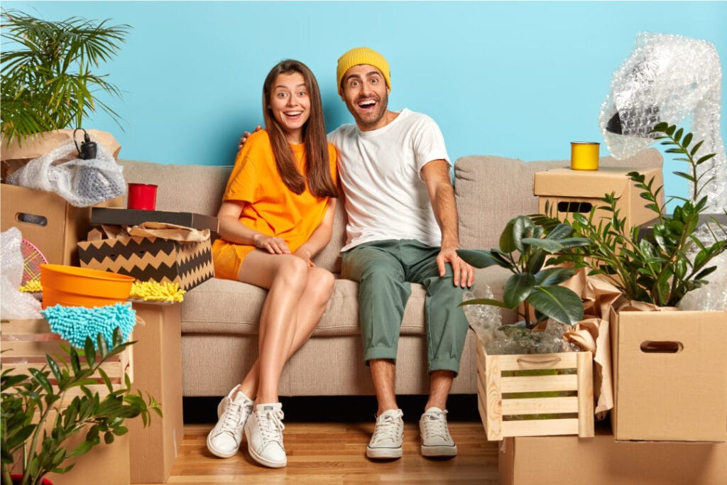 glad husband wife look with happiness hug while sit sofa living room move new home cardboard boxes around